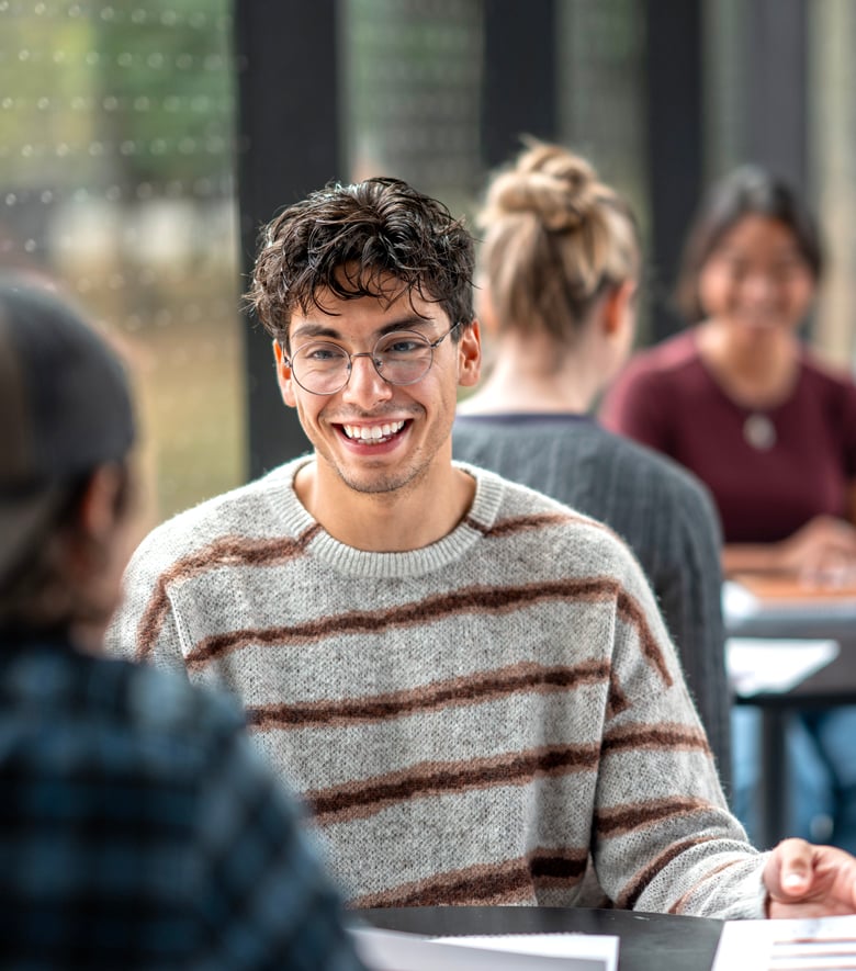 Smiling student in a striped sweater talking with classmates at a table